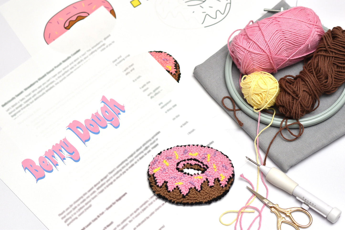 Punch needle donut coaster with yarn, scissors, and a pattern sheet on a white background