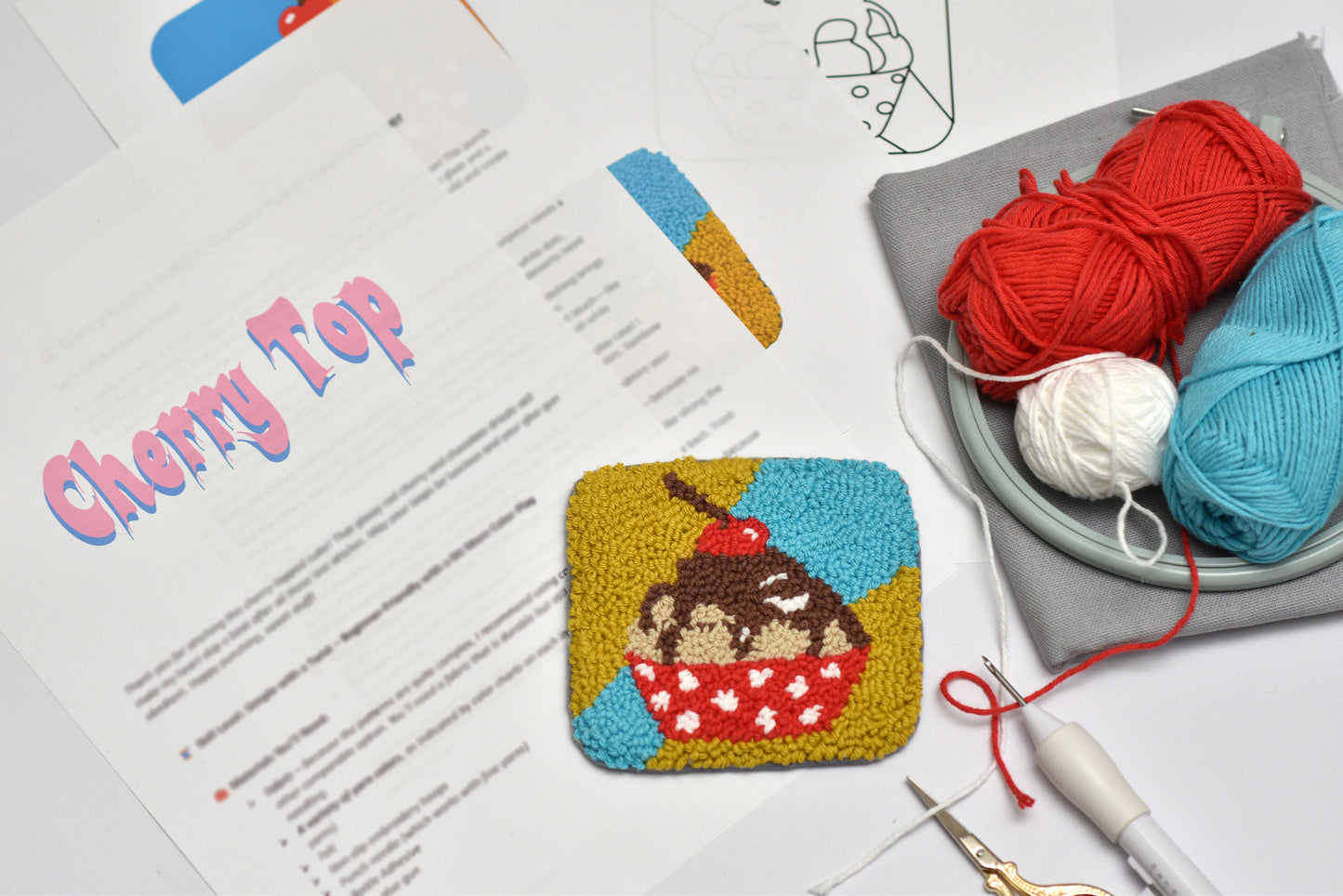 Punch needle coaster cup cake design with yarn and tools on a table