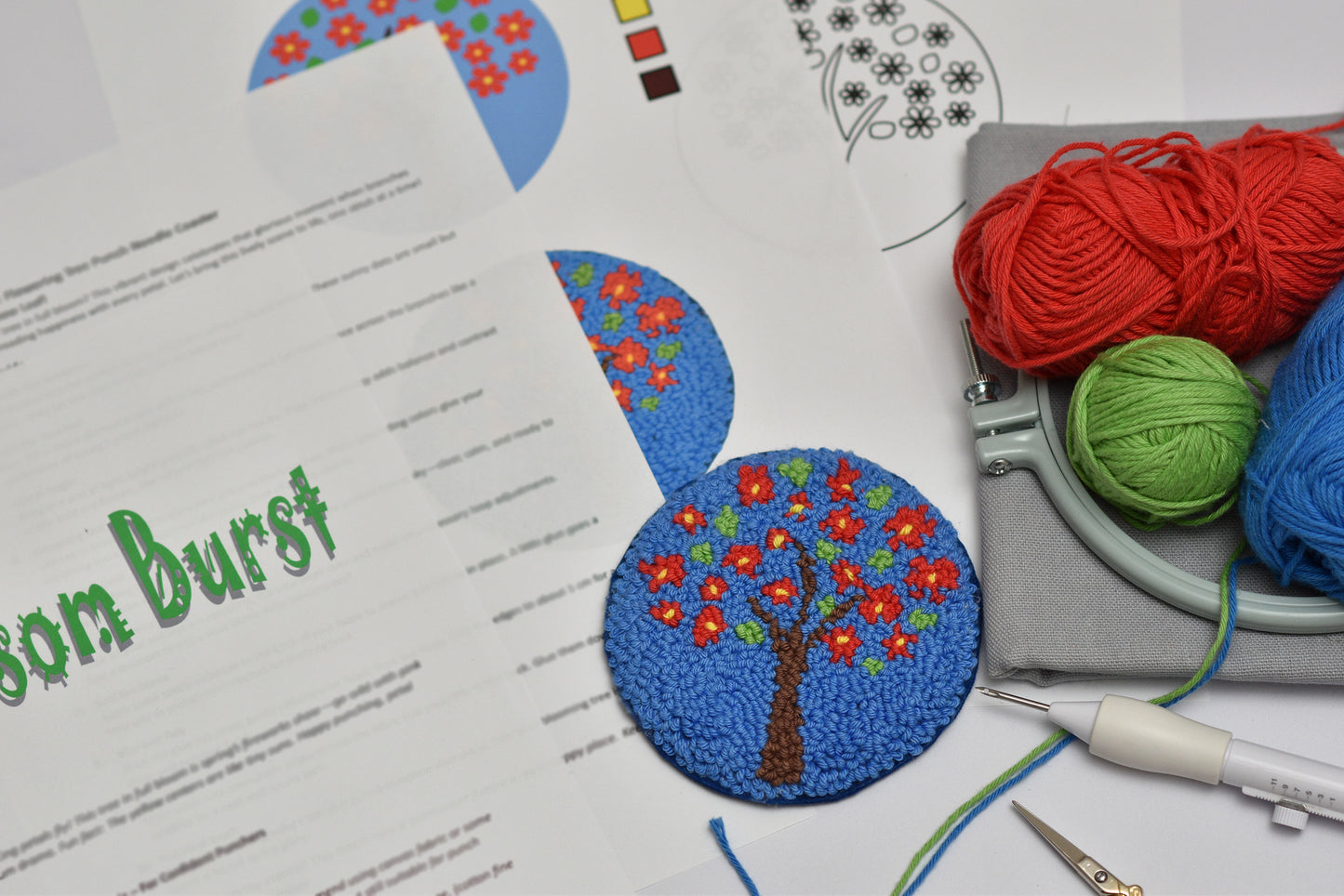 Embroidery hoop and a coaster design featuring red flowers and green leaves, yarn, and sewing tools on a table