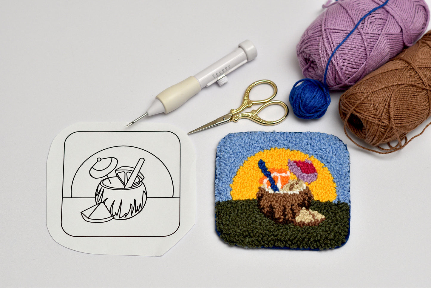 Crocheted coaster with a coconut and sun design, next to yarn and tools on a light gray background