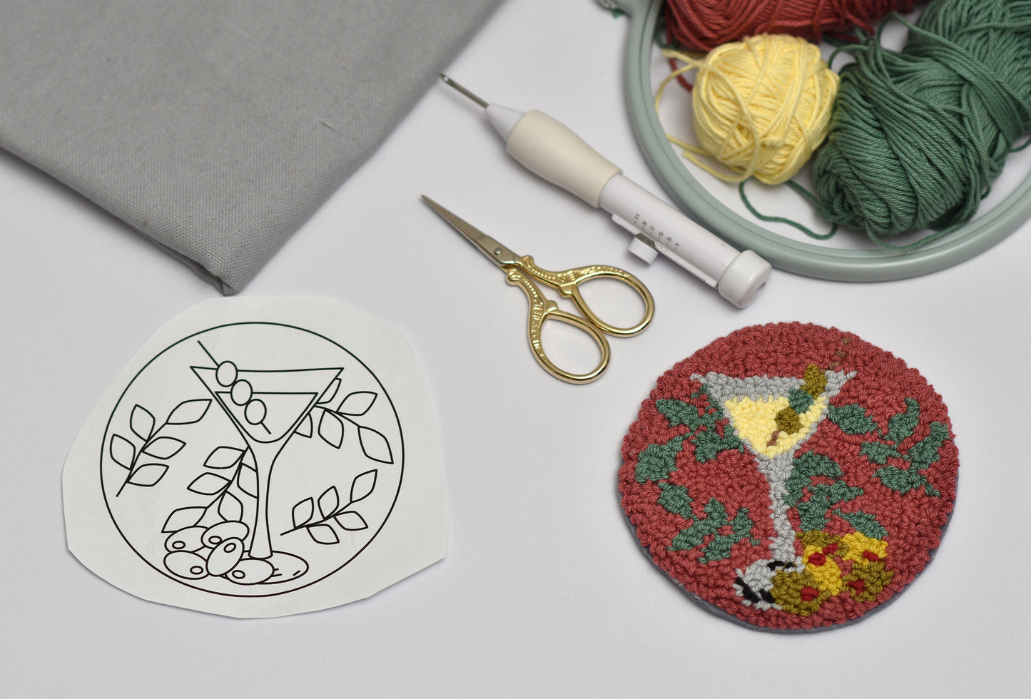 Embroidery hoop with yarn, scissors, and punch needled coaster with Martini design