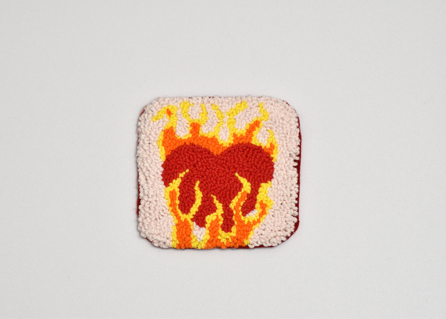 Square punch needle coater with a heart design in flames on a light gray background