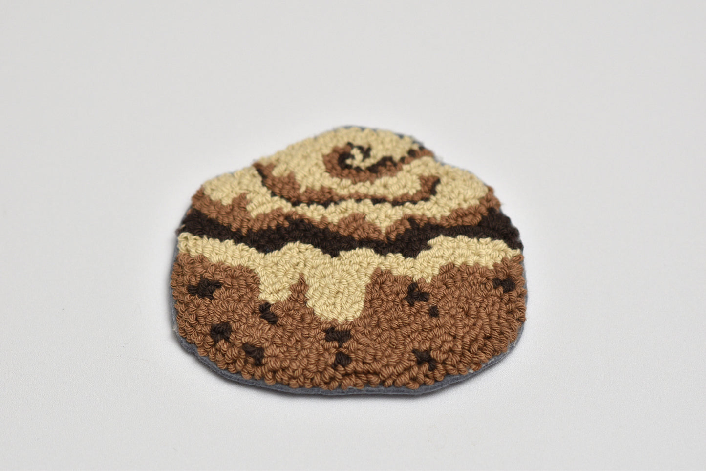 Brown and beige colored cinnamon roll design coaster on a light gray background