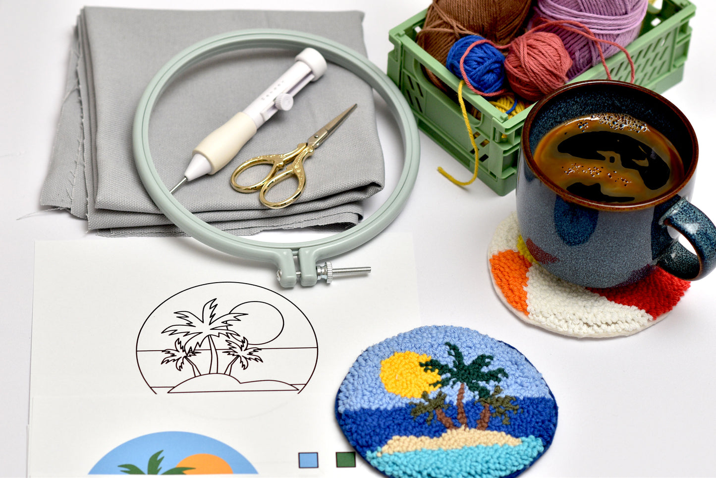 Embroidery hoop, fabric, scissors, yarn, and a mug with coasters on a table.