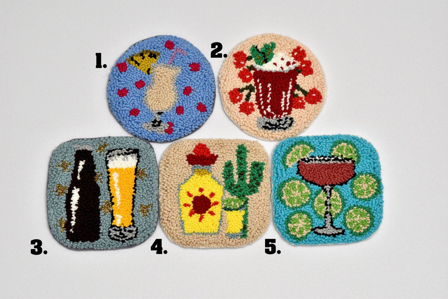 Five colorful embroidered coasters with various designs (pineapple colada, cherry cooler, Beer Glass, Tequila and Lime, Cosmopolitan)on a light gray background