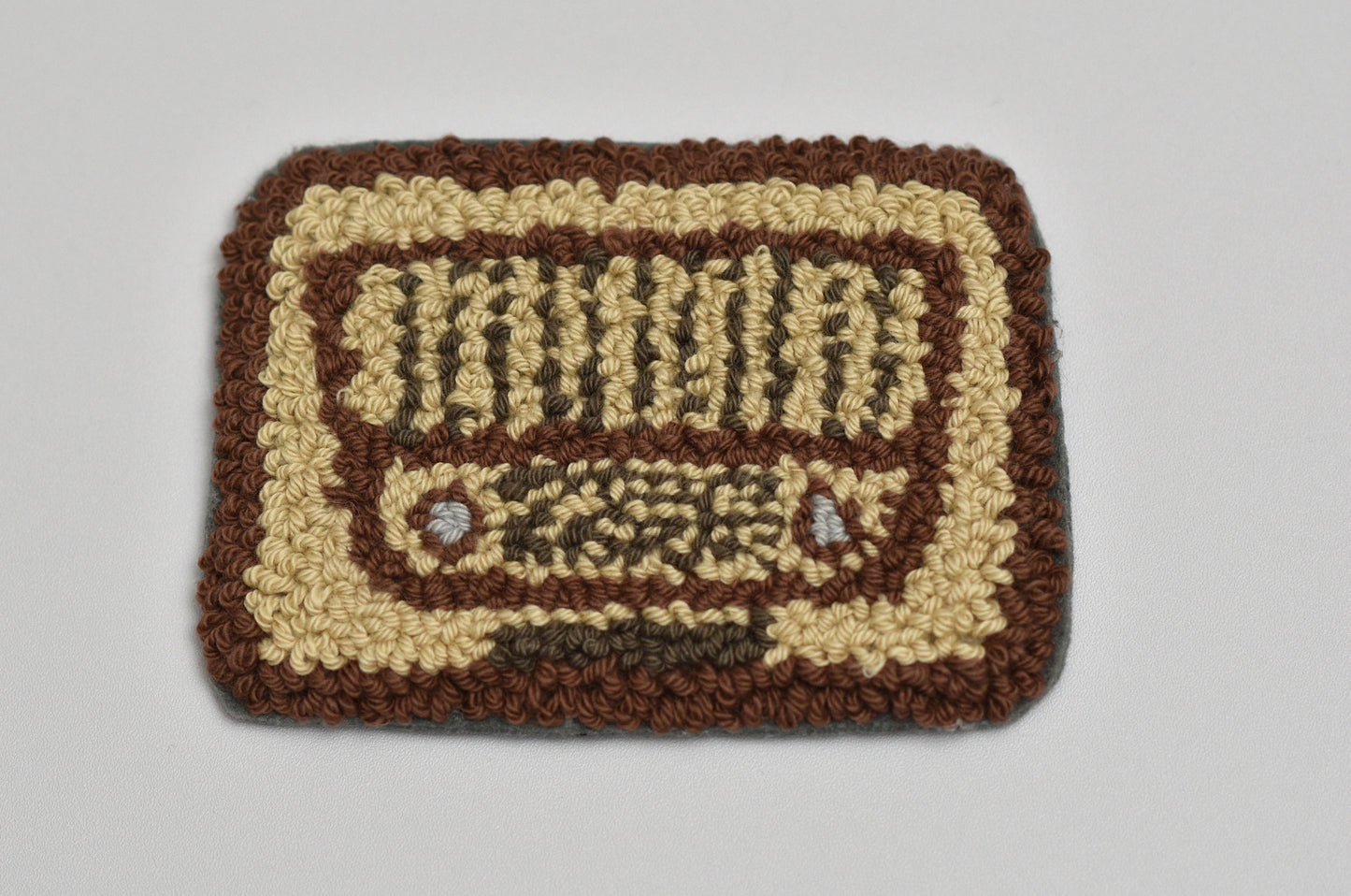 Handmade punch needle coaster with a radio design on a plain background
