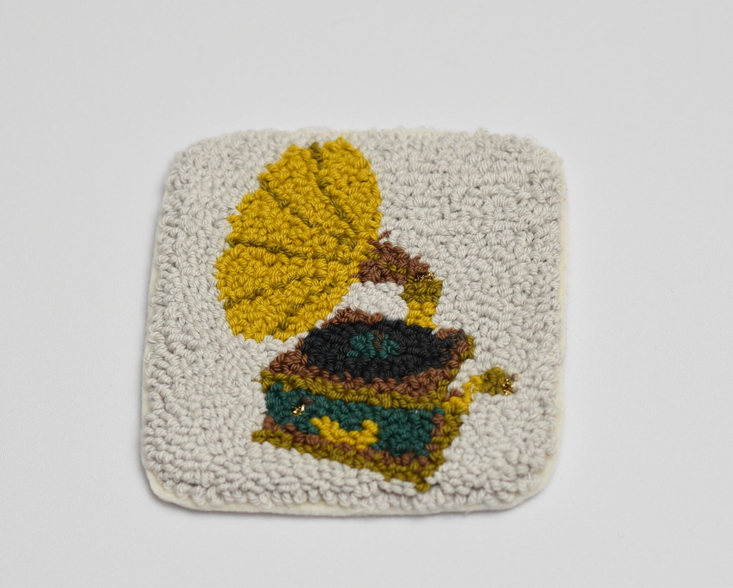 Square punch needle coaster with a gramophone design on a light gray background