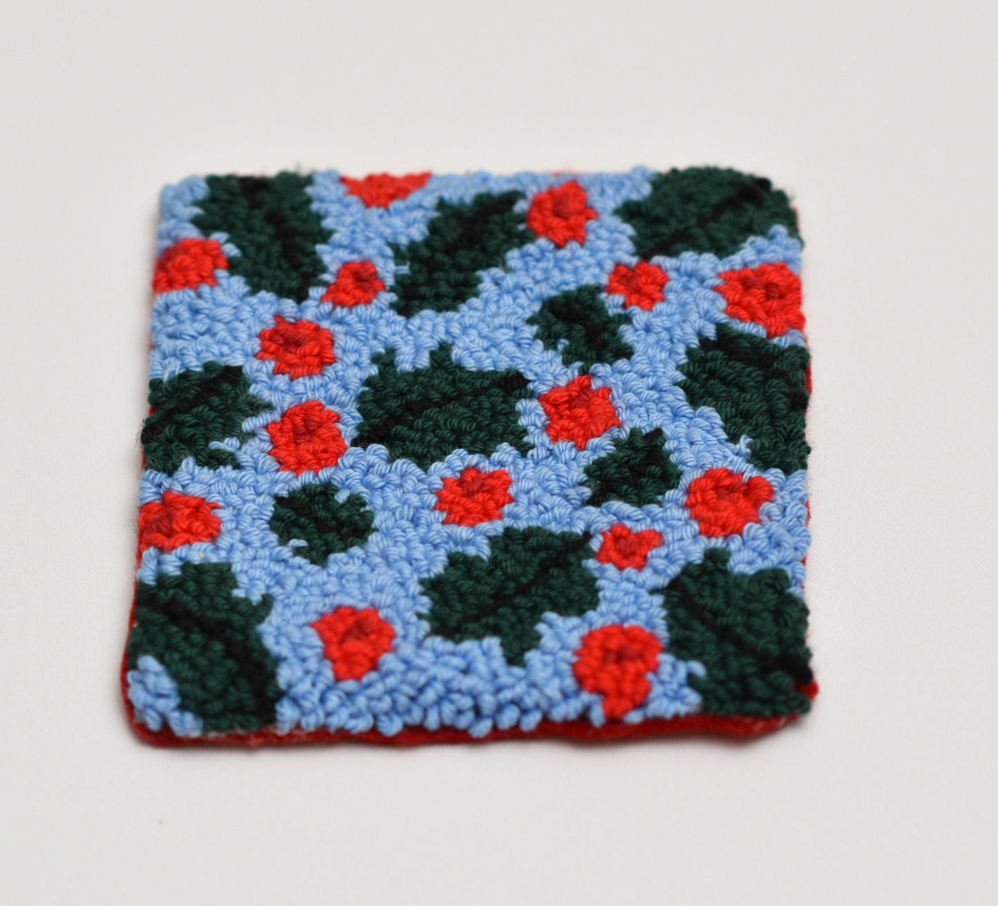 Embroidered square coaster with red and green mistletoe pattern on a light gray background