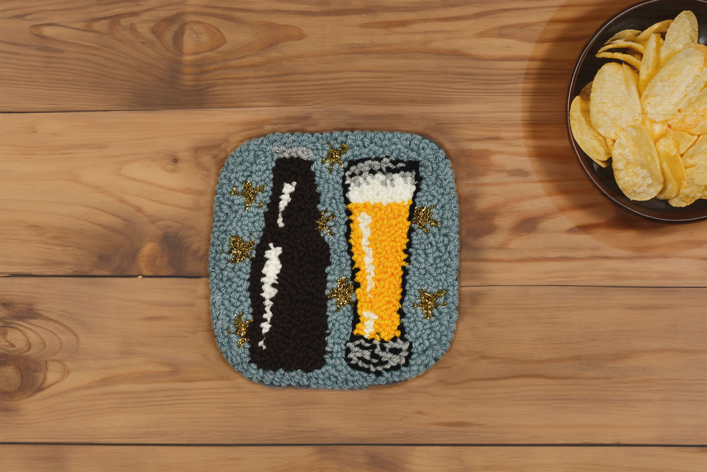 Textured coaster with beer bottle and glass design on a wooden surface with chips.