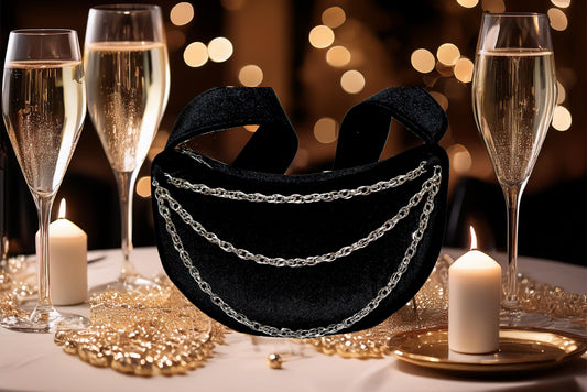 Black velvet bag with silver chains on a table with champagne glasses and candles.
