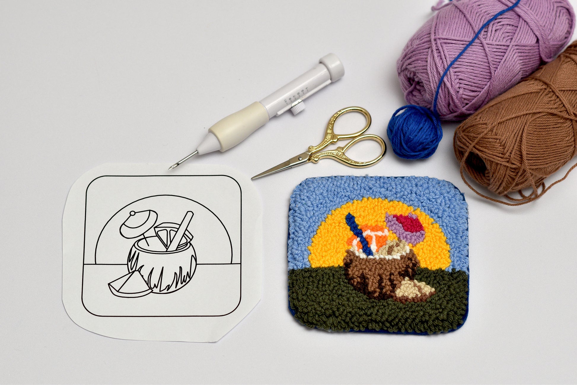 Crocheted coaster with a coconut and sun design, next to yarn and tools on a light gray background