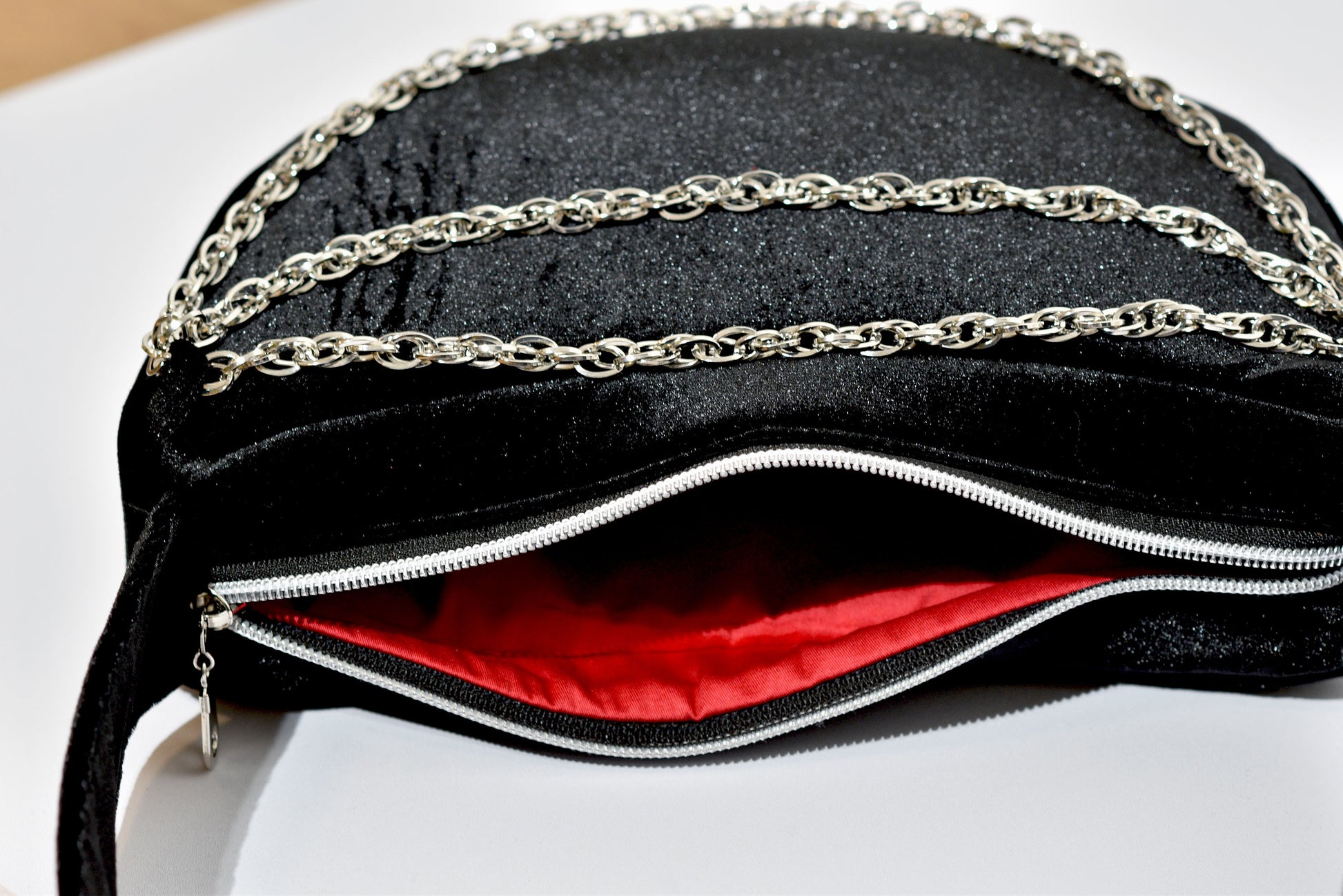 Black velvet evening bag with chain detail and red lining on a white background