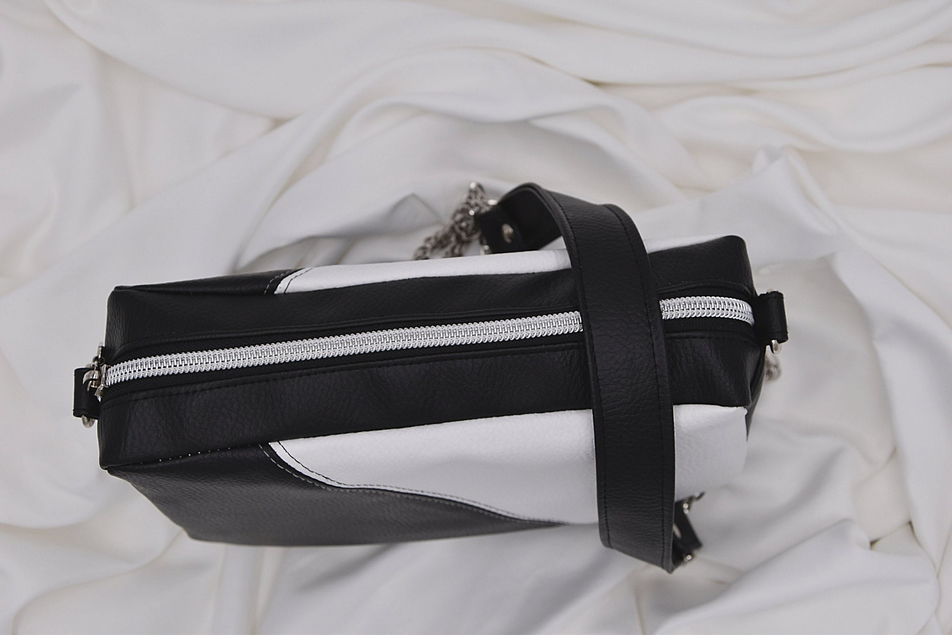 Overlook showing zipper of Black and white faux leather shoulder bag with chain and leather strap