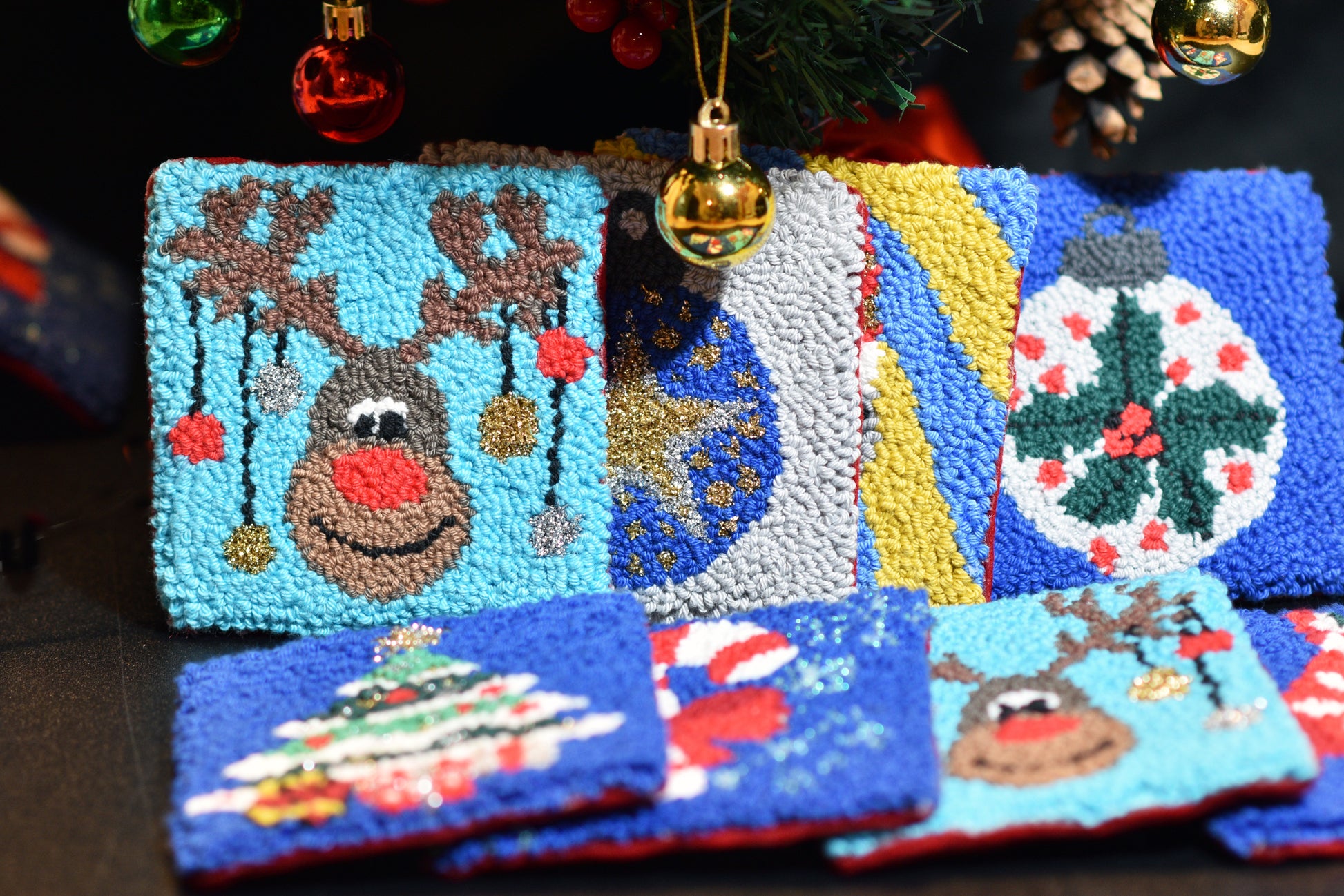 Several Christmas punch needle mug rugs in front of a Christmas decoration and tree